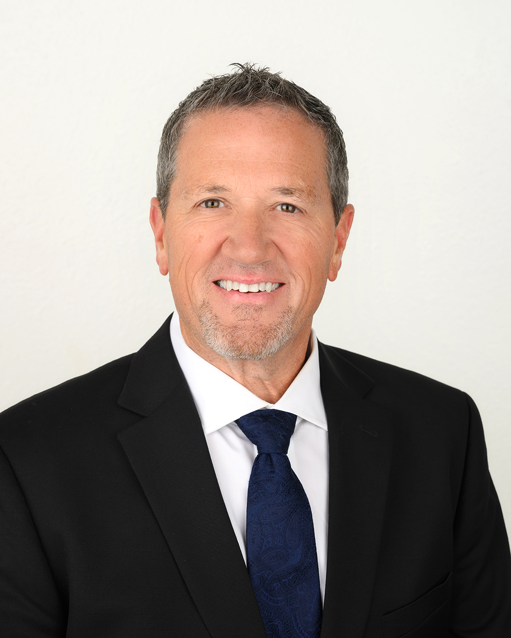 Man smiling in professional dark suit, white shirt, navy tie