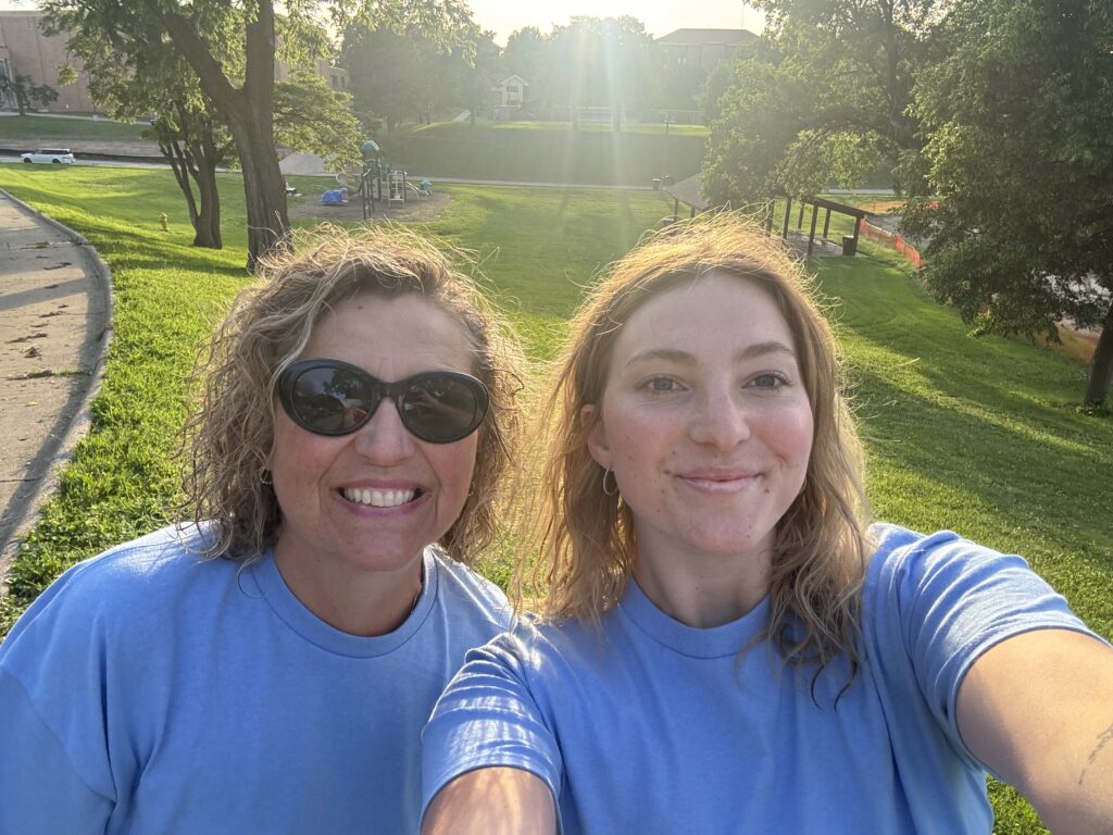 A realtor in sunglasses and her daughter smiling in blue shirts at trash clean up