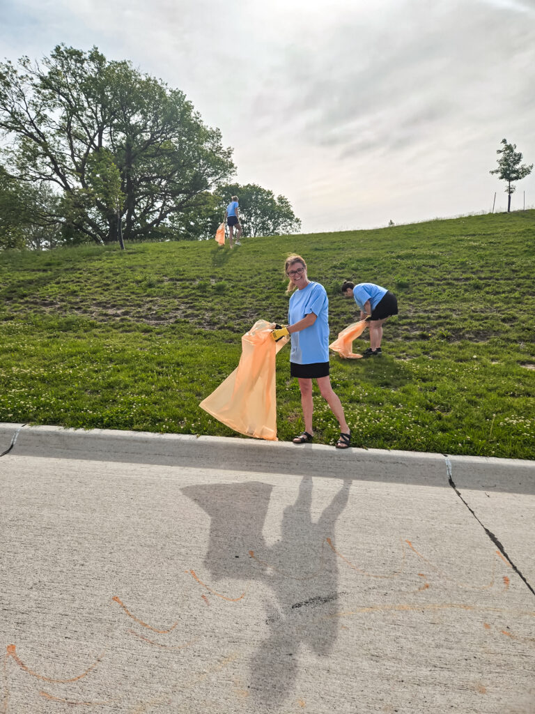 Person picking up trash in an orange bag while the wind blows it