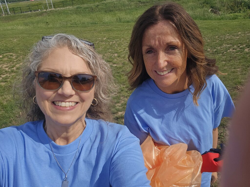 Two realtors smiling in a selfie picture while picking up trash