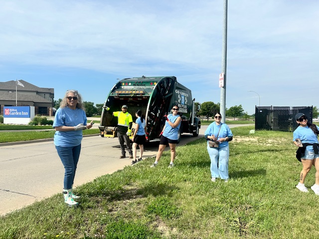 Five realtors in blue shirts are near a garbage truck picking up trash